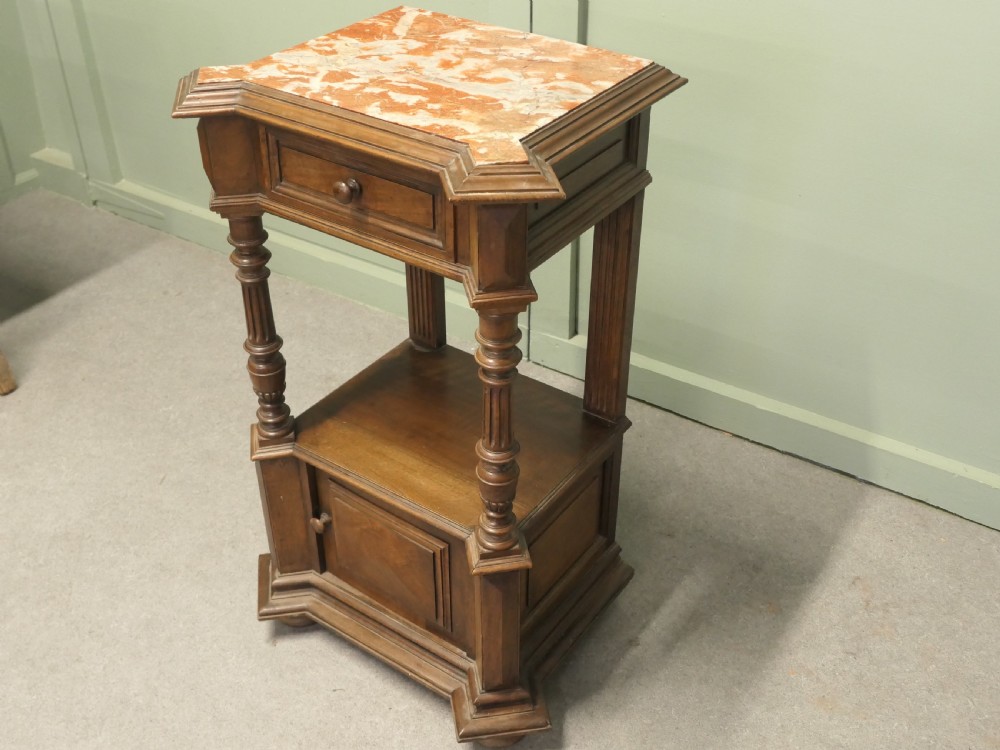 A 19th-century French walnut side cabinet with a pink marble inset top, a single upper drawer, turned columns, an open shelf, and a lower cupboard door. View VI