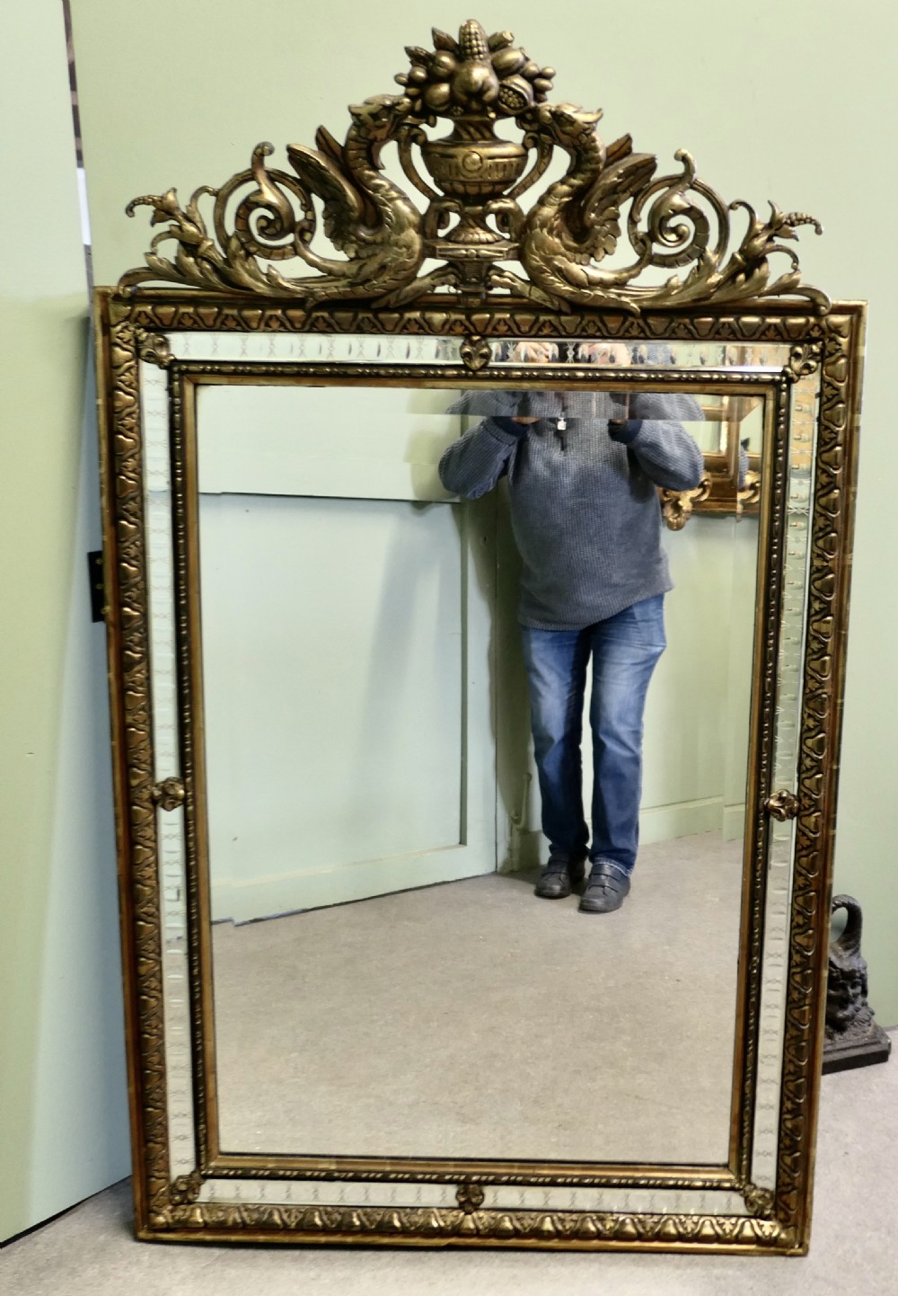 A large rectangular French giltwood wall mirror featuring ornate cresting carved with dragons and an urn above mirrored border margins.