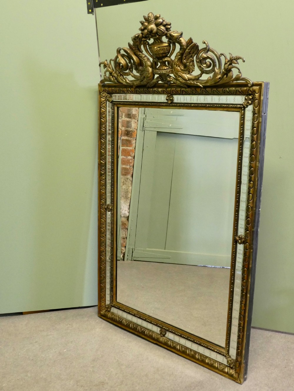 A large rectangular French giltwood wall mirror featuring ornate cresting carved with dragons and an urn above mirrored border margins. View II