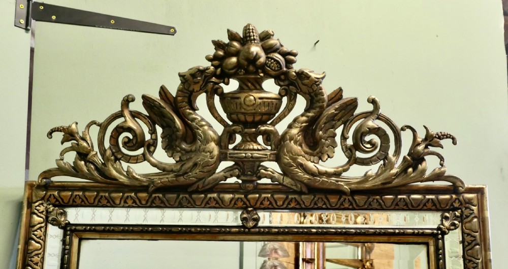 A large rectangular French giltwood wall mirror featuring ornate cresting carved with dragons and an urn above mirrored border margins. View III