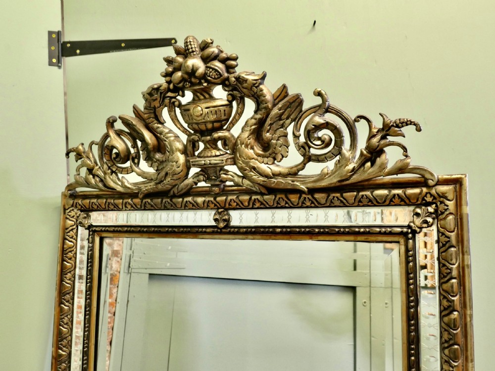 A large rectangular French giltwood wall mirror featuring ornate cresting carved with dragons and an urn above mirrored border margins. View V