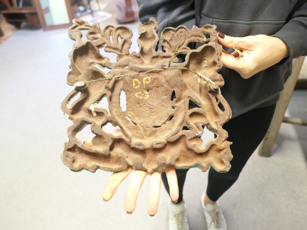 A painted cast iron wall plaque featuring the British Royal Coat of Arms with a gold lion and white unicorn supporting a quartered shield. View VI