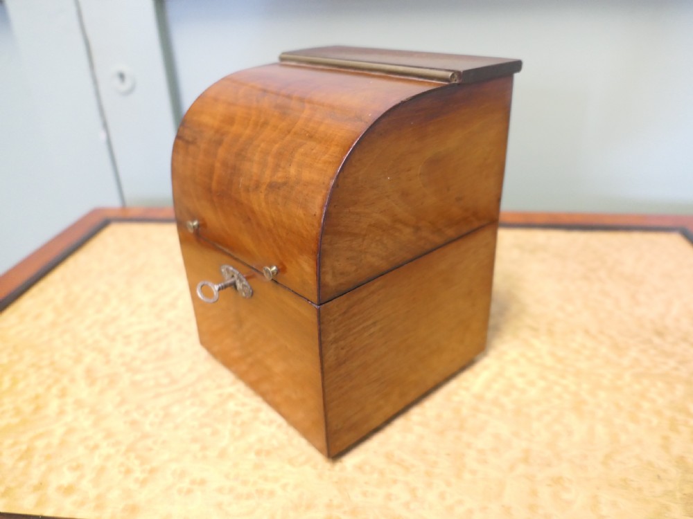 A 19th-century wooden decanter box featuring a curved top, warm brown grain, brass fittings, and a key inserted into the front lock.
