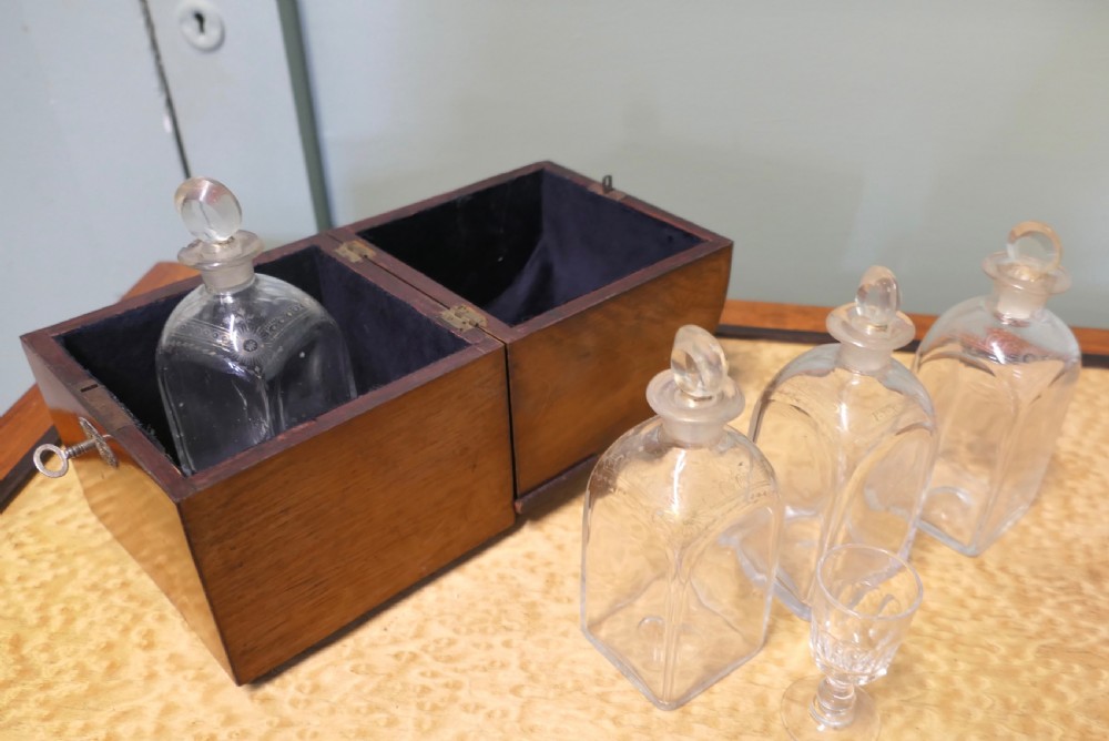 A 19th-century wooden decanter box featuring a curved top, warm brown grain, brass fittings, and a key inserted into the front lock. View V