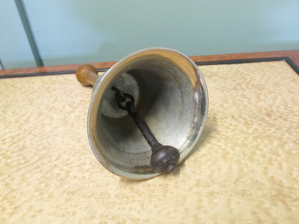 An antique brass hand bell featuring a flared metal skirt, a turned wooden handle, and a brass finial top. View II