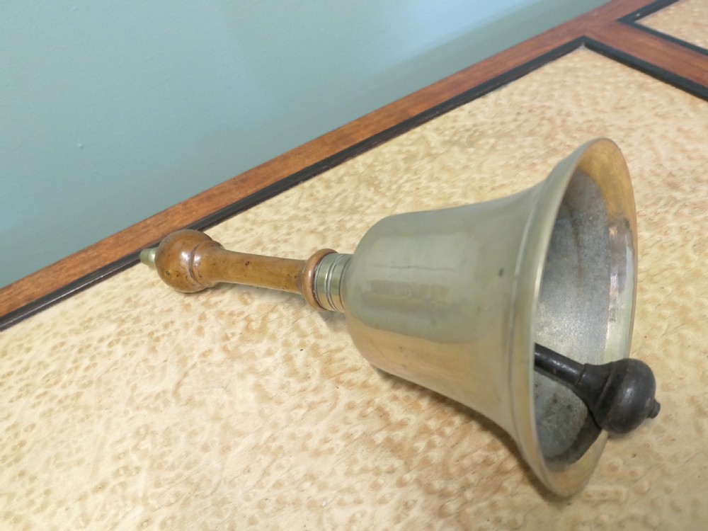 An antique brass hand bell featuring a flared metal skirt, a turned wooden handle, and a brass finial top. View III