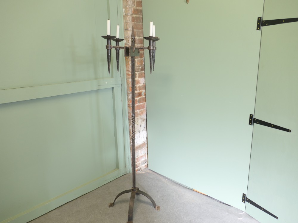 A tall wrought iron floor-standing candelabra featuring a twisted central stem, an arched four-legged base, and five candle holders on crossbars. View II