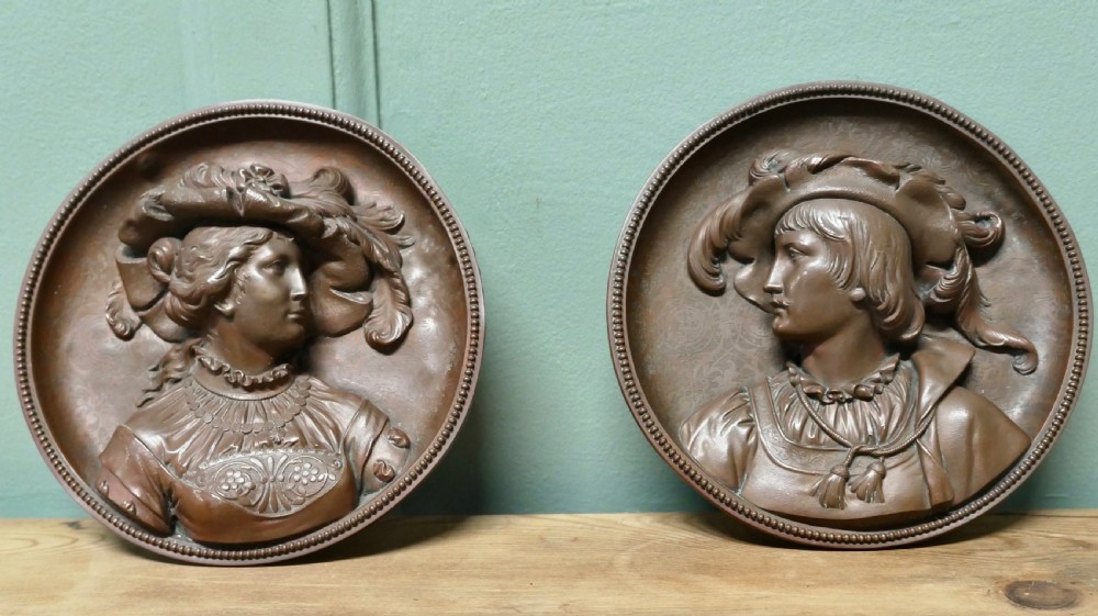 A pair of circular 19th-century copper wall plaques featuring raised relief portraits of a man and a woman in Renaissance attire within beaded borders.