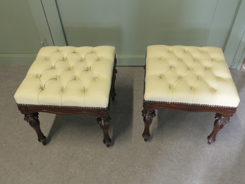 A pair of square deep-buttoned cream leather stools set on carved turned walnut legs with brass studding along the frames.