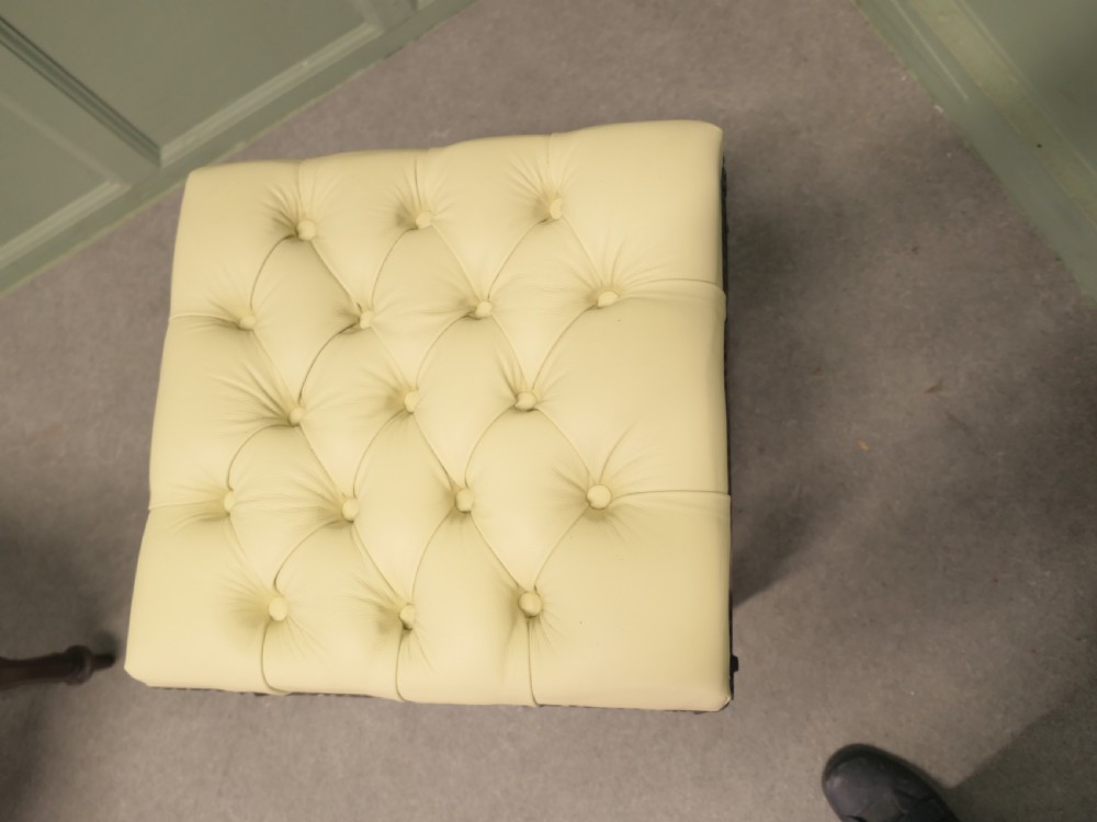 A pair of square deep-buttoned cream leather stools set on carved turned walnut legs with brass studding along the frames. View VII