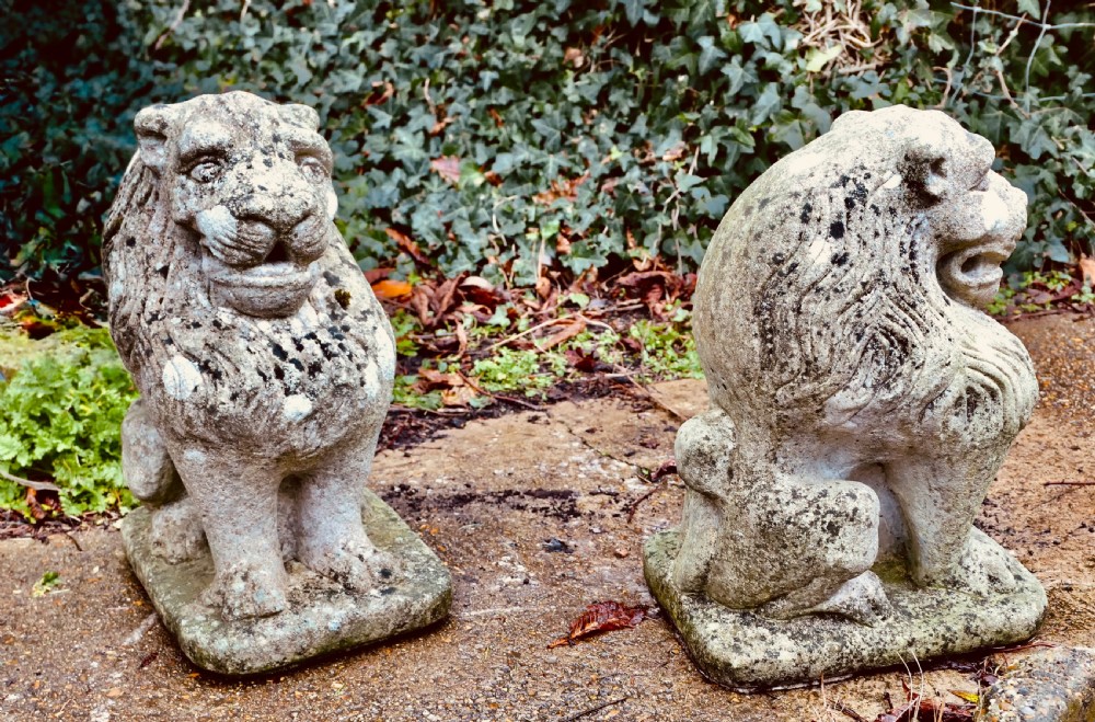 A pair of weathered cast stone lion statues depicted sitting upright on rectangular integral bases with visible lichen patination. View VII