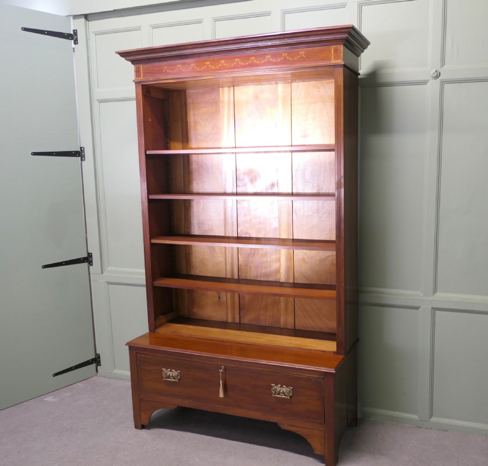 A tall Edwardian open walnut bookcase featuring an inlaid decorative frieze, four adjustable shelves, and a single wide base drawer with brass handles.