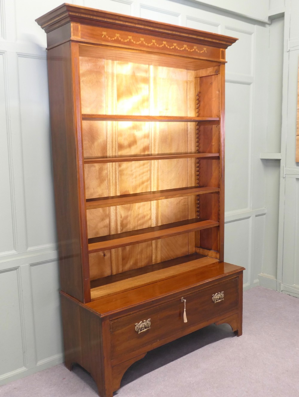 A tall Edwardian open walnut bookcase featuring an inlaid decorative frieze, four adjustable shelves, and a single wide base drawer with brass handles. View III