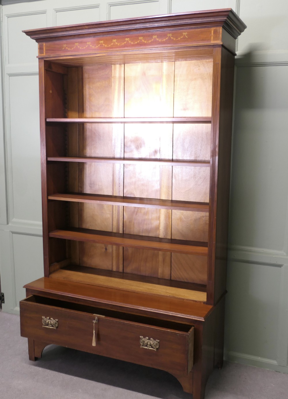 A tall Edwardian open walnut bookcase featuring an inlaid decorative frieze, four adjustable shelves, and a single wide base drawer with brass handles. View V