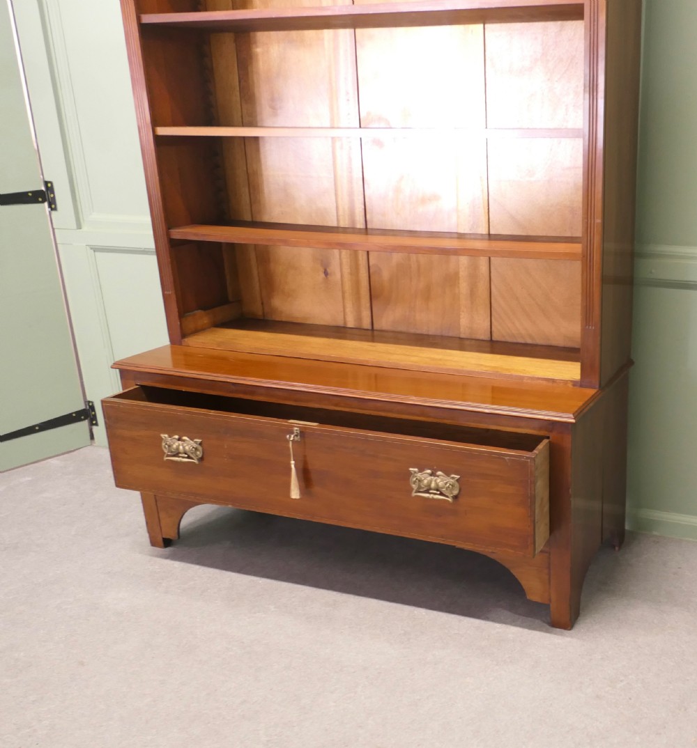 A tall Edwardian open walnut bookcase featuring an inlaid decorative frieze, four adjustable shelves, and a single wide base drawer with brass handles. View VI