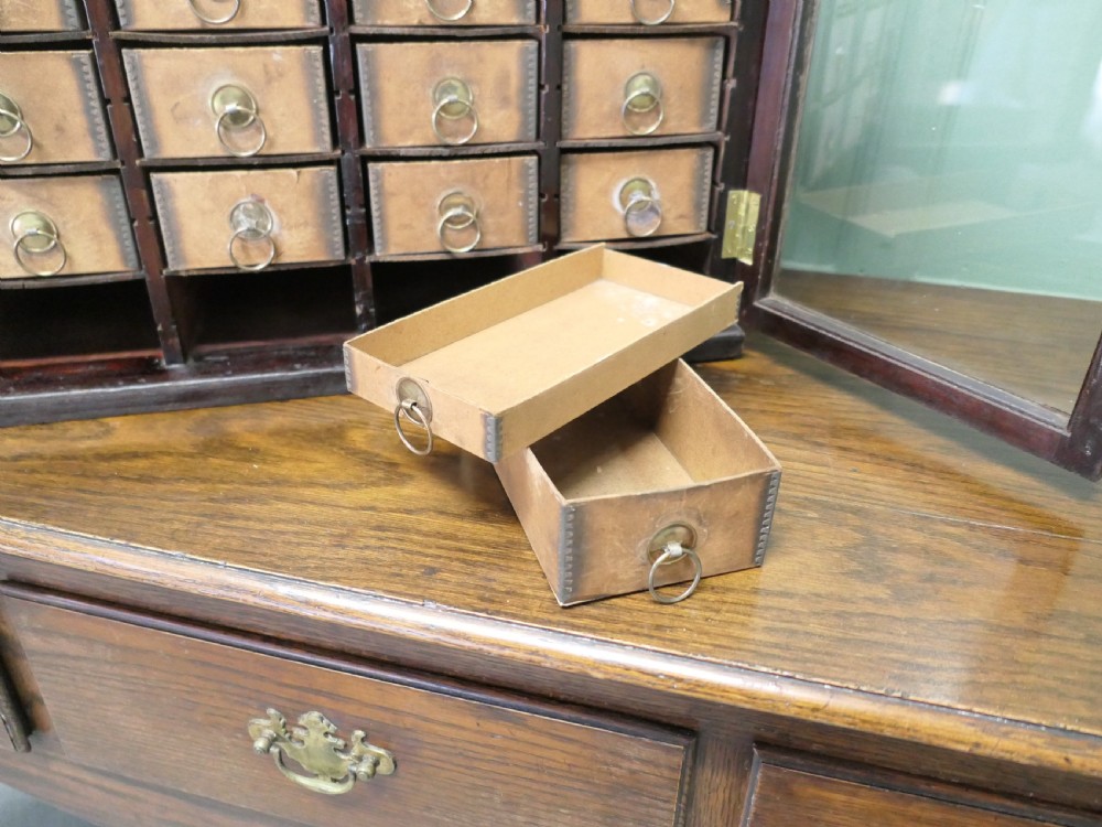 A dark wood glazed haberdashery cabinet featuring twin glass doors enclosing twenty-eight small drawers with brass ring pulls. View V