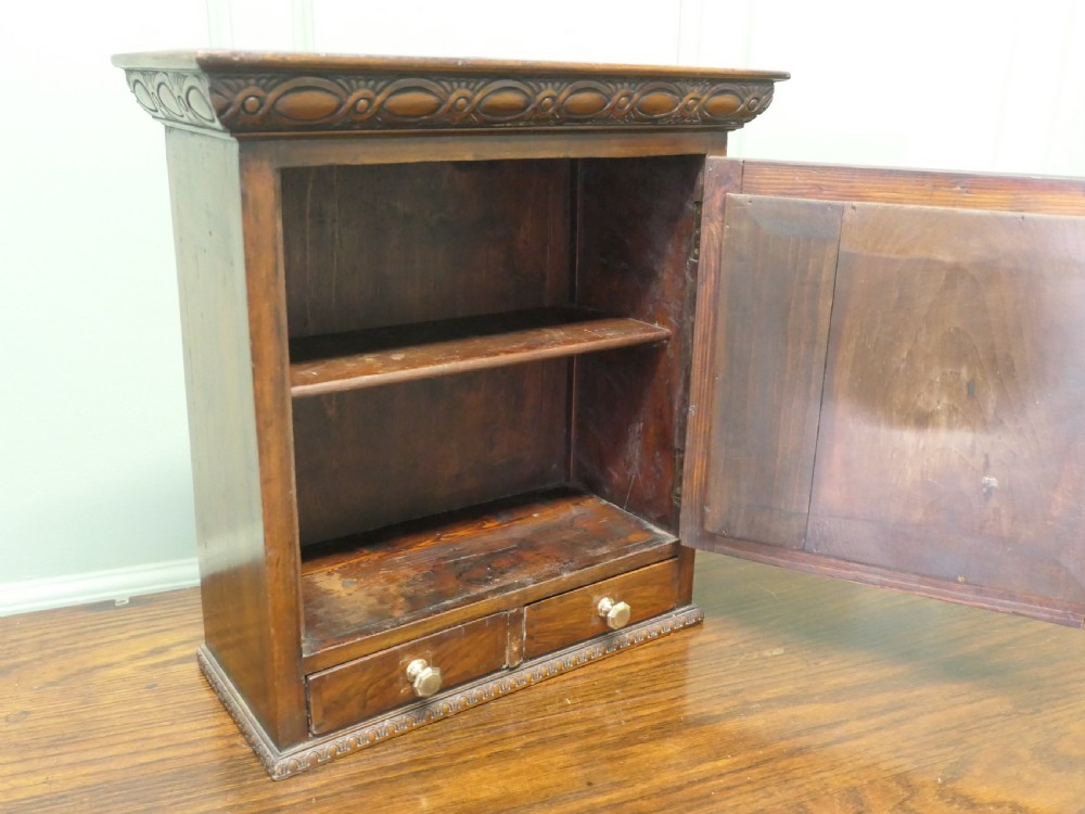 A small burr walnut cabinet featuring a single door with a central circular veneer inlay positioned above two lower drawers with round brass knobs. View IV