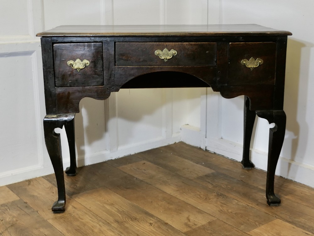 An 18th-century dark oak lowboy featuring three drawers with brass handles, an arched apron, and cabriole legs. View III