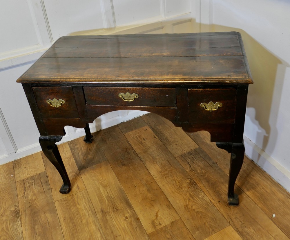 An 18th-century dark oak lowboy featuring three drawers with brass handles, an arched apron, and cabriole legs. View V