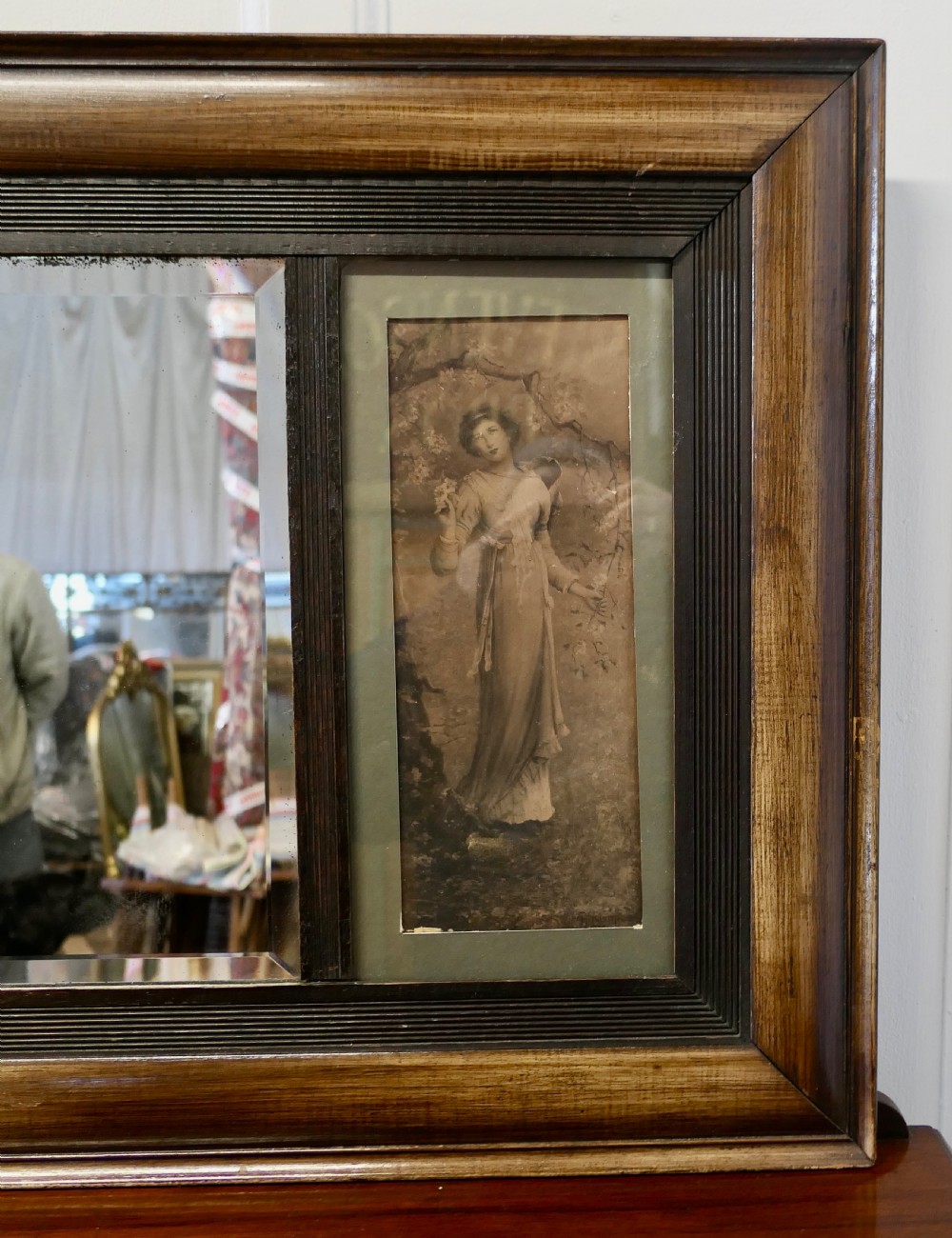 An Edwardian rectangular wooden wall mirror featuring a central mirror plate flanked by two framed vertical prints of women. View V
