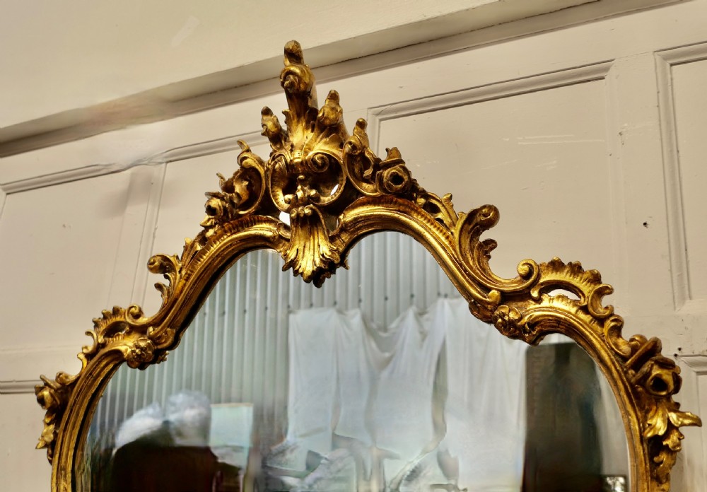 An ornate French Rococo style giltwood console table featuring a contoured white marble top beneath a matching gilded pier mirror with elaborate scroll carving. View V