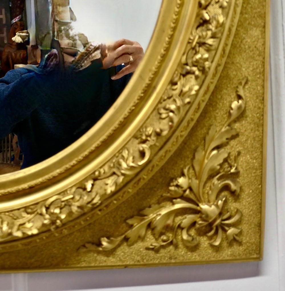 A rectangular gilded wood mirror frame featuring a central oval aperture with beaded detail and acanthus leaf corner mouldings. View V