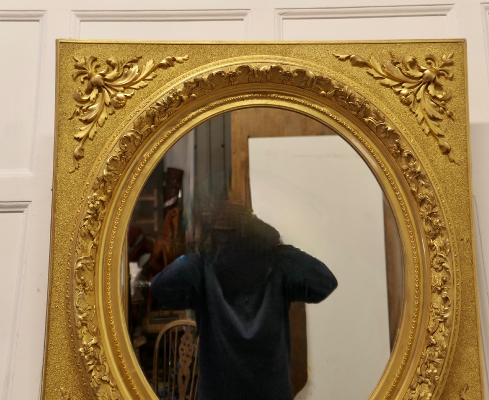 A rectangular gilded wood mirror frame featuring a central oval aperture with beaded detail and acanthus leaf corner mouldings. View VII