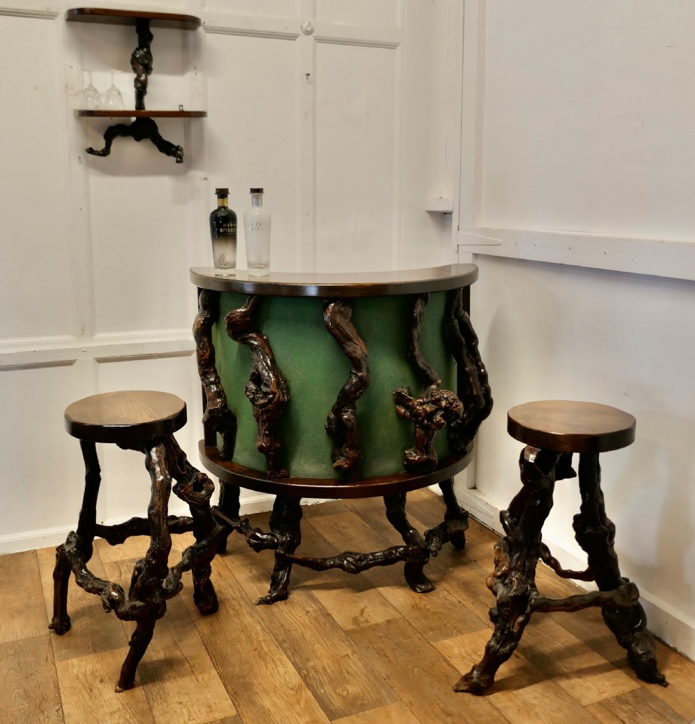 A curved home bar constructed from gnarled grapevine roots with a green padded front, accompanied by two matching round-topped bar stools.