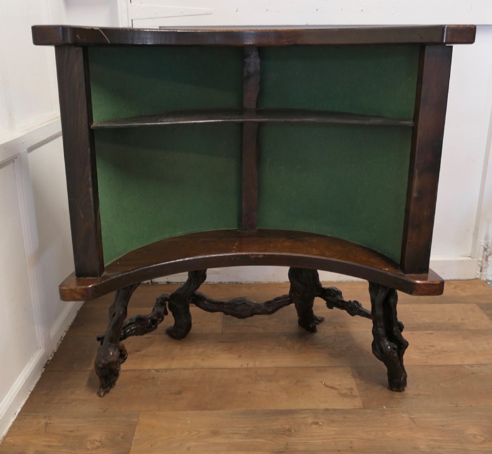 A curved home bar constructed from gnarled grapevine roots with a green padded front, accompanied by two matching round-topped bar stools. View VII