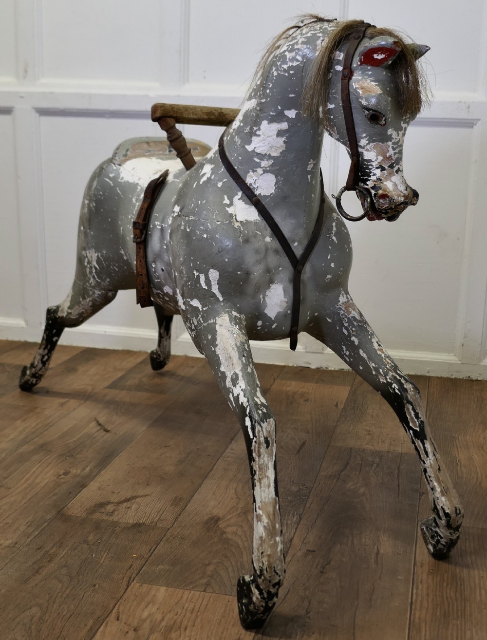 An early 19th-century hand-carved wooden horse featuring a distressed grey and white painted finish with leather harness and horsehair detail.