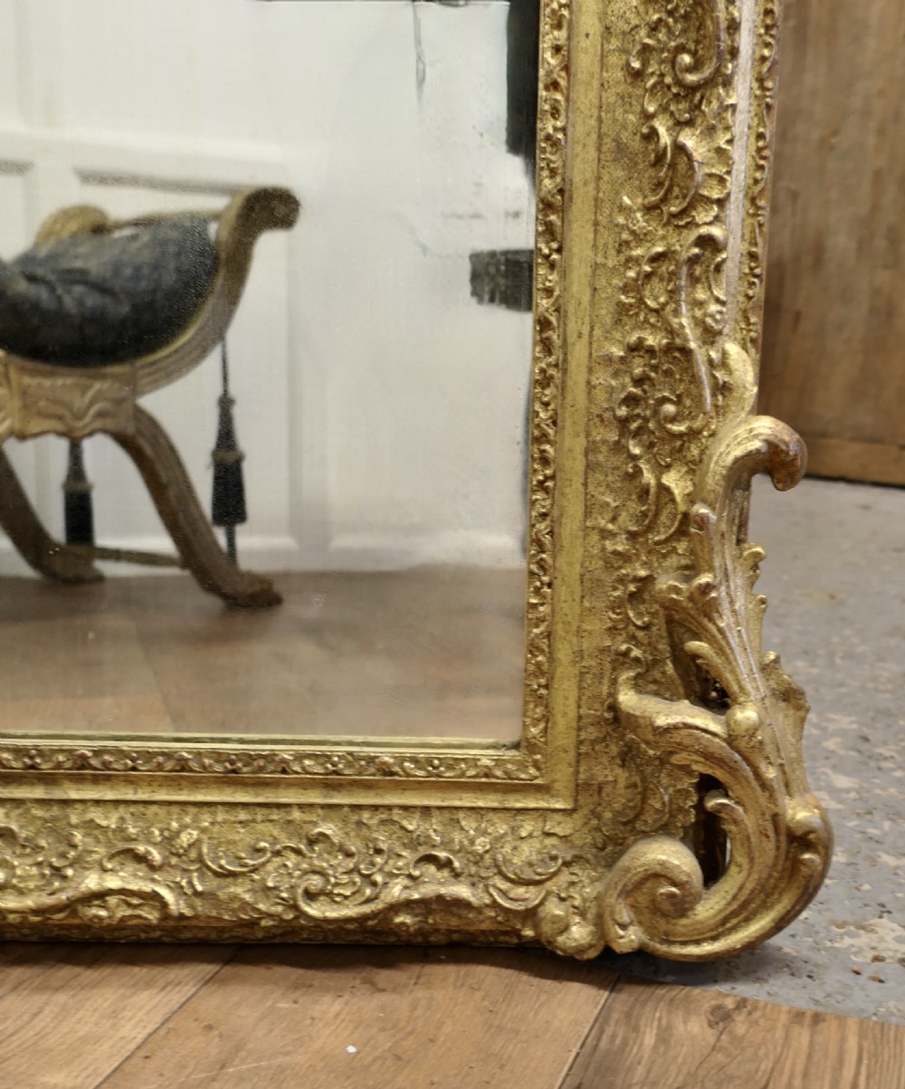 A large French Louis Philippe giltwood wall mirror featuring an ornate floral cresting pediment and carved scrolling foliage along the frame. View III