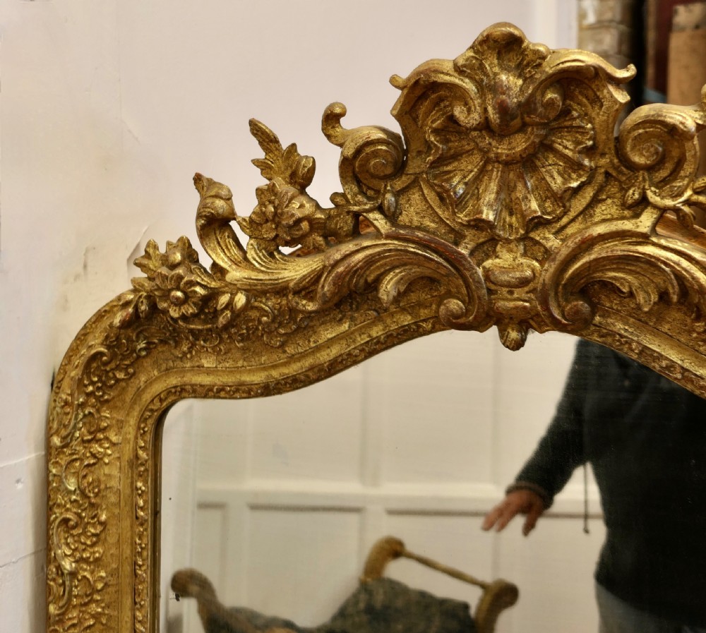 A large French Louis Philippe giltwood wall mirror featuring an ornate floral cresting pediment and carved scrolling foliage along the frame. View VII