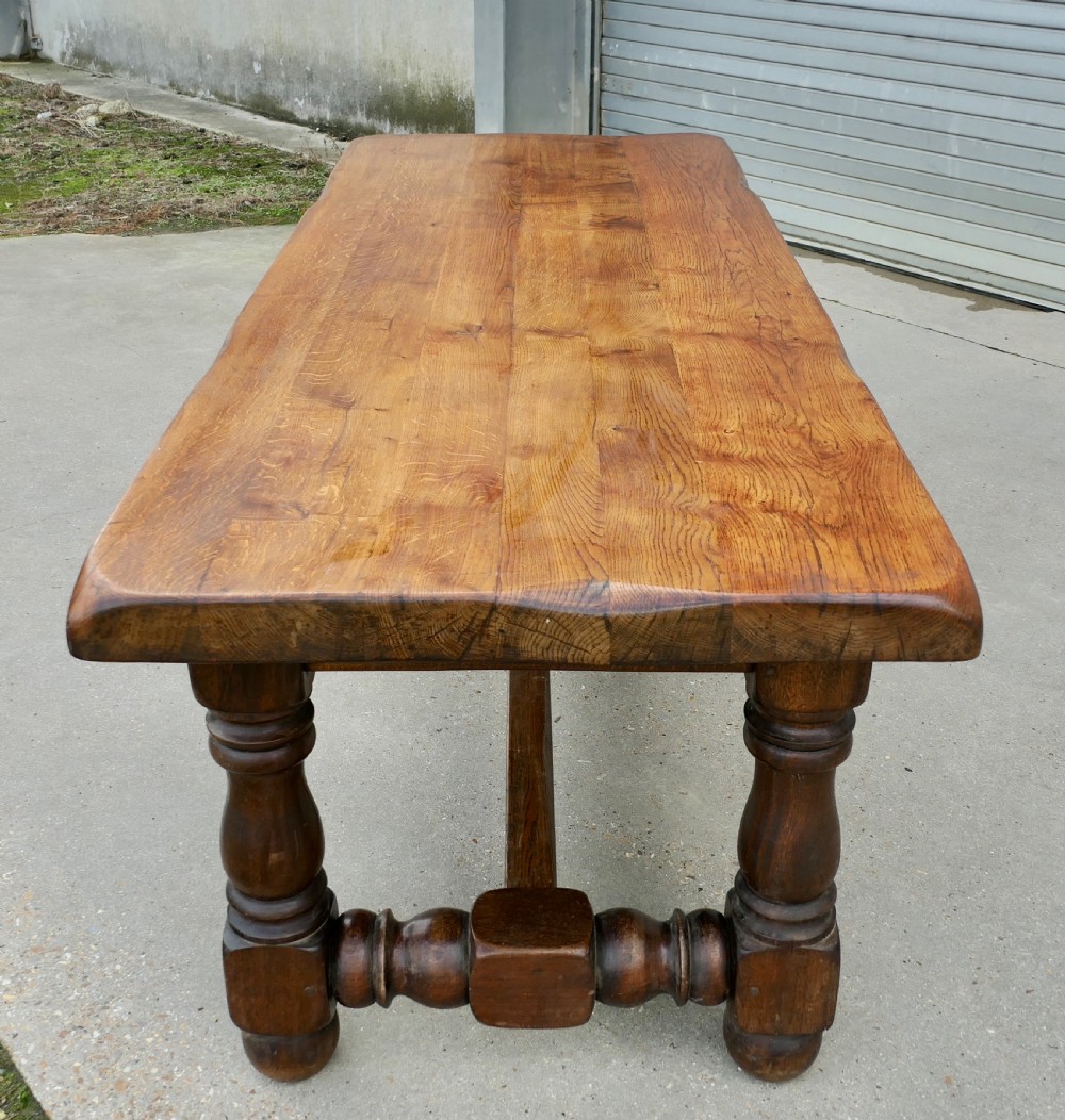 A large solid oak refectory dining table featuring a thick plank top, heavy turned baluster legs, and a low central stretcher base.