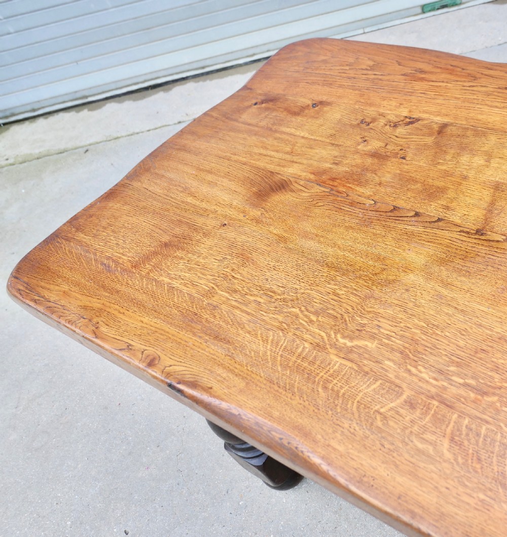 A large solid oak refectory dining table featuring a thick plank top, heavy turned baluster legs, and a low central stretcher base. View III