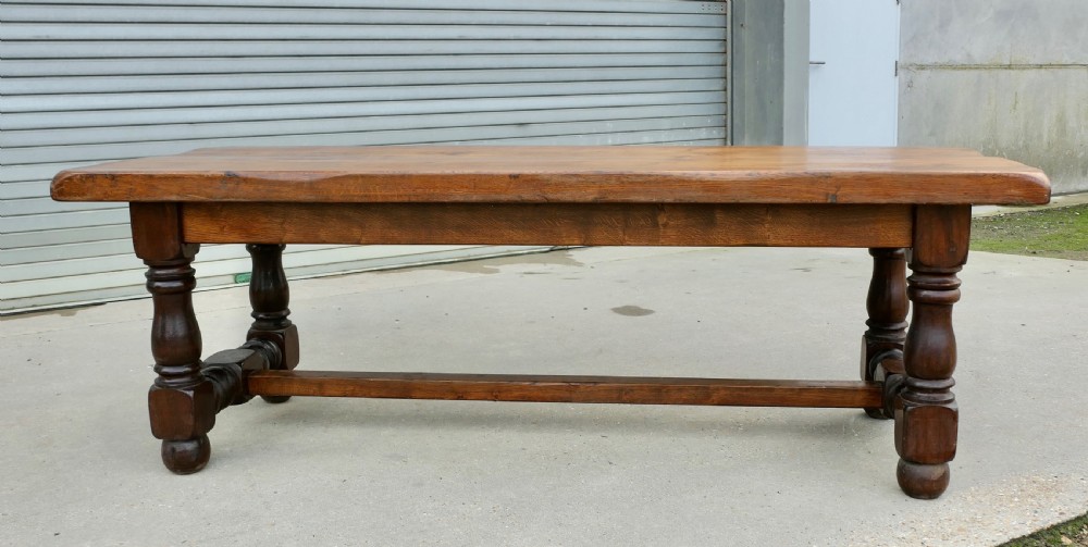 A large solid oak refectory dining table featuring a thick plank top, heavy turned baluster legs, and a low central stretcher base. View VII