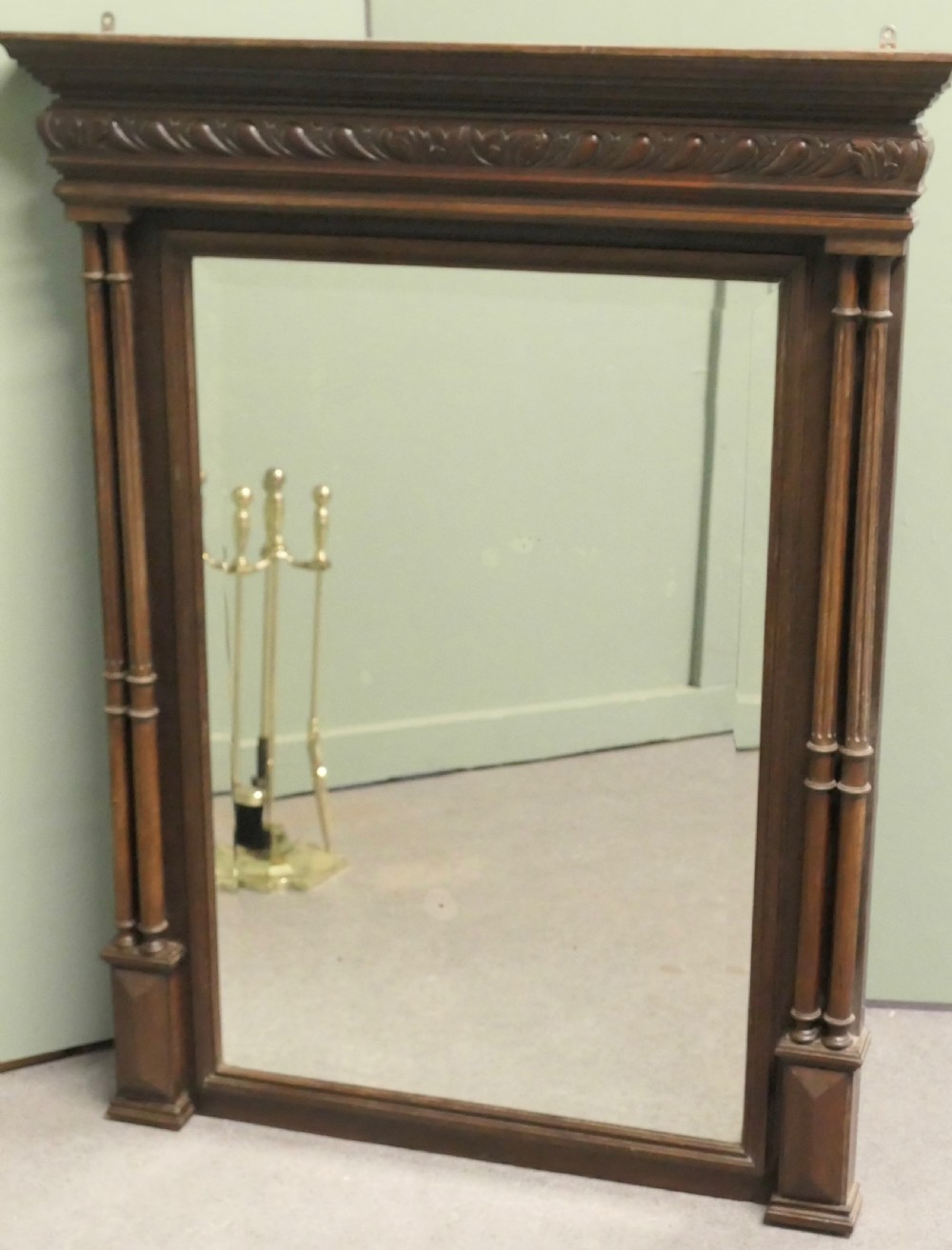 A dark oak rectangular wall mirror featuring an architectural carved cornice and twin slender columns flanking the glass plate.