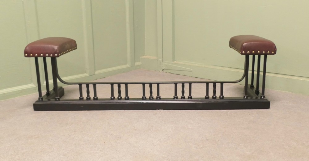 An Art Deco style club fender featuring a black iron frame with twisted vertical spindles and two elevated tan leather padded seats trimmed with studs. View II