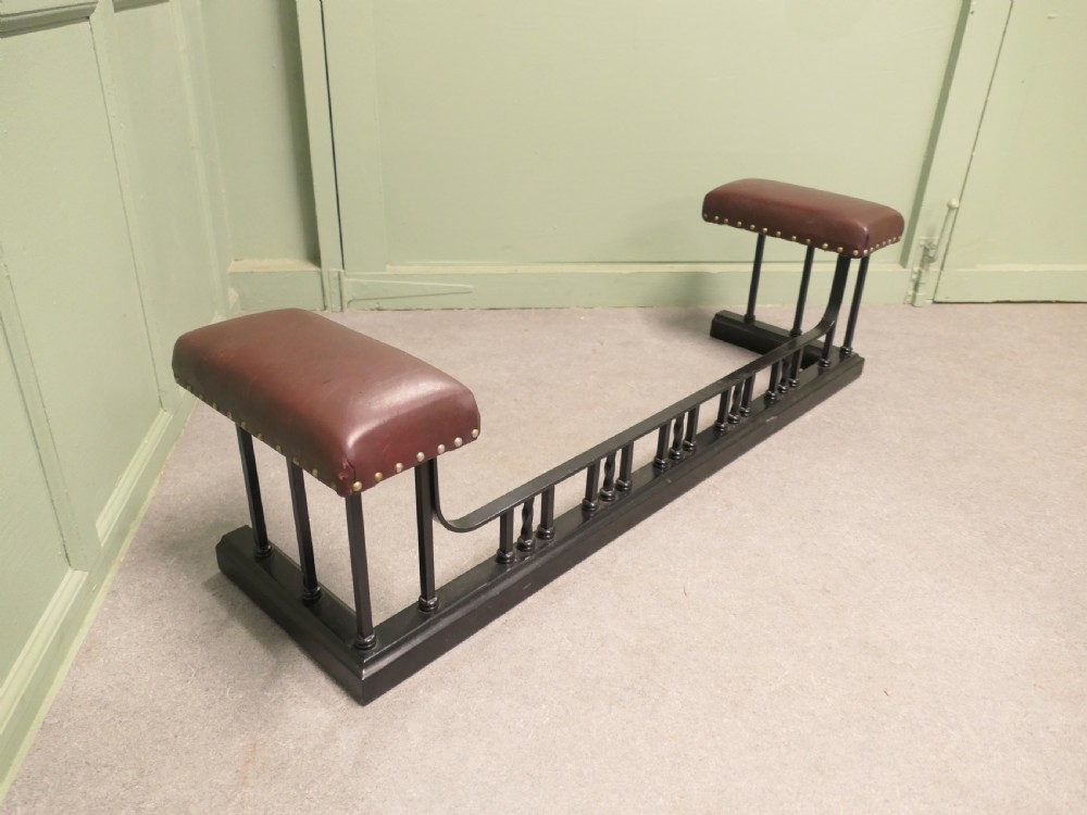 An Art Deco style club fender featuring a black iron frame with twisted vertical spindles and two elevated tan leather padded seats trimmed with studs. View IV