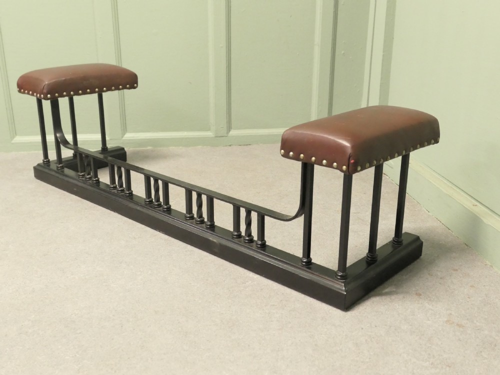 An Art Deco style club fender featuring a black iron frame with twisted vertical spindles and two elevated tan leather padded seats trimmed with studs. View V