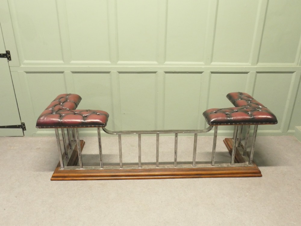 A Victorian brass club fender featuring vertical metal spindles, deep-buttoned red leather corner seats, and a moulded wooden base.