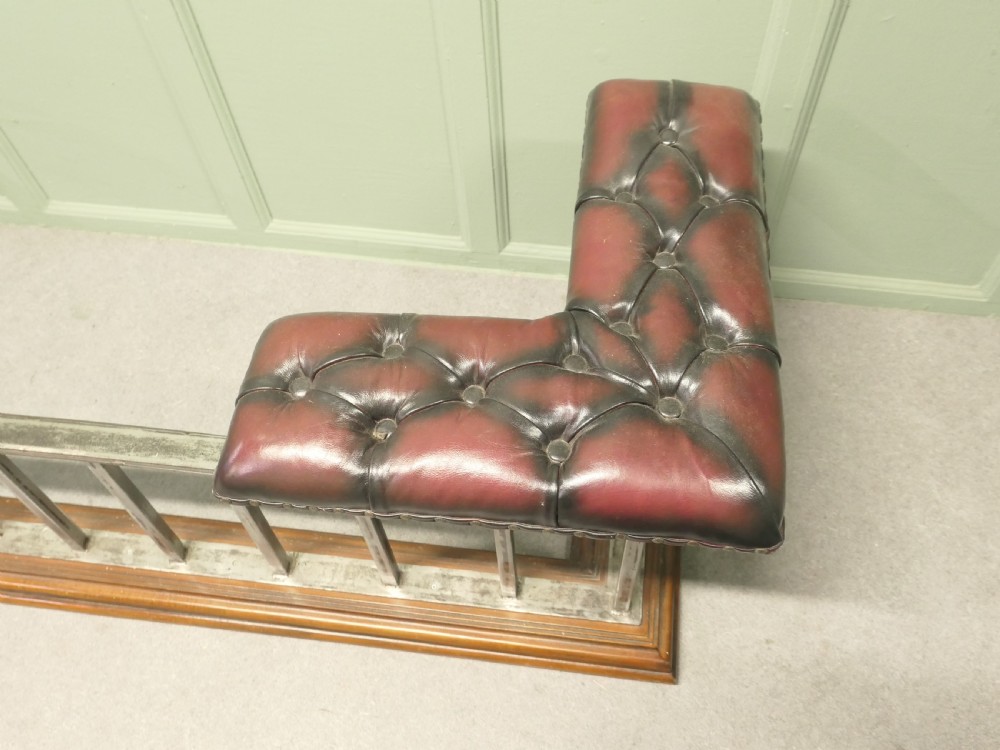 A Victorian brass club fender featuring vertical metal spindles, deep-buttoned red leather corner seats, and a moulded wooden base. View II