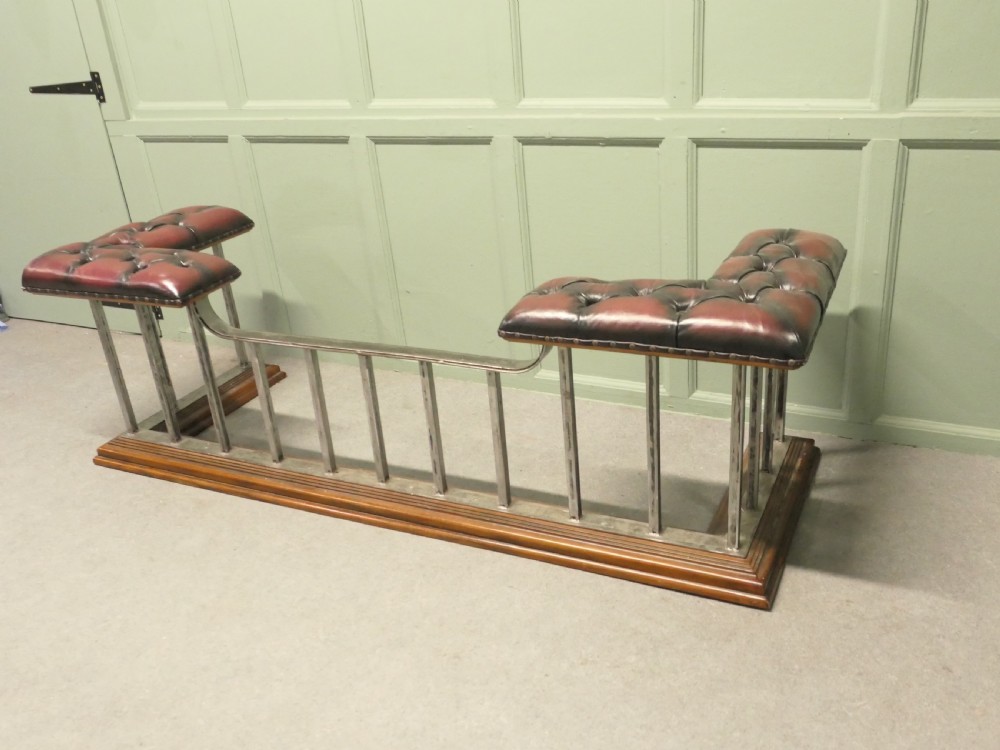 A Victorian brass club fender featuring vertical metal spindles, deep-buttoned red leather corner seats, and a moulded wooden base. View IV