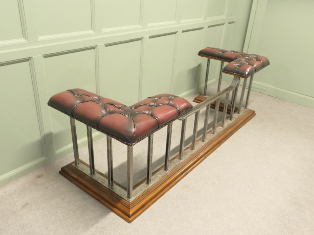 A Victorian brass club fender featuring vertical metal spindles, deep-buttoned red leather corner seats, and a moulded wooden base. View V
