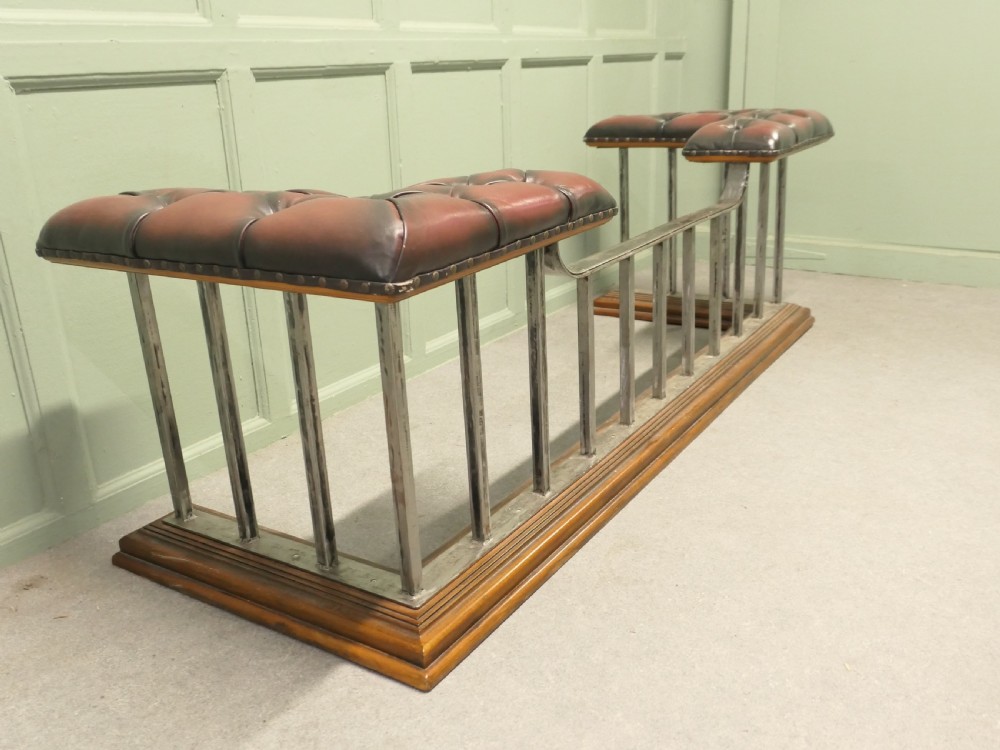 A Victorian brass club fender featuring vertical metal spindles, deep-buttoned red leather corner seats, and a moulded wooden base. View VI