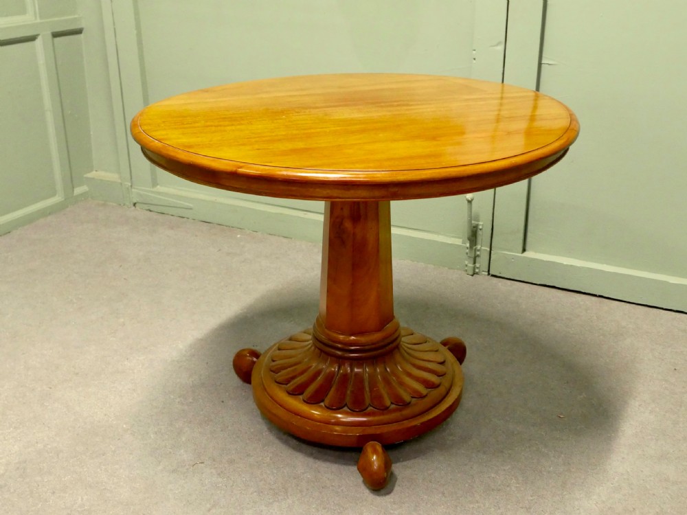 A circular cherrywood centre table featuring a polished tilt-top surface, a central stem, and a carved petal-form pedestal base on ball feet.