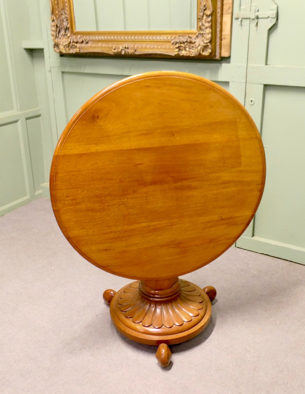 A circular cherrywood centre table featuring a polished tilt-top surface, a central stem, and a carved petal-form pedestal base on ball feet. View II