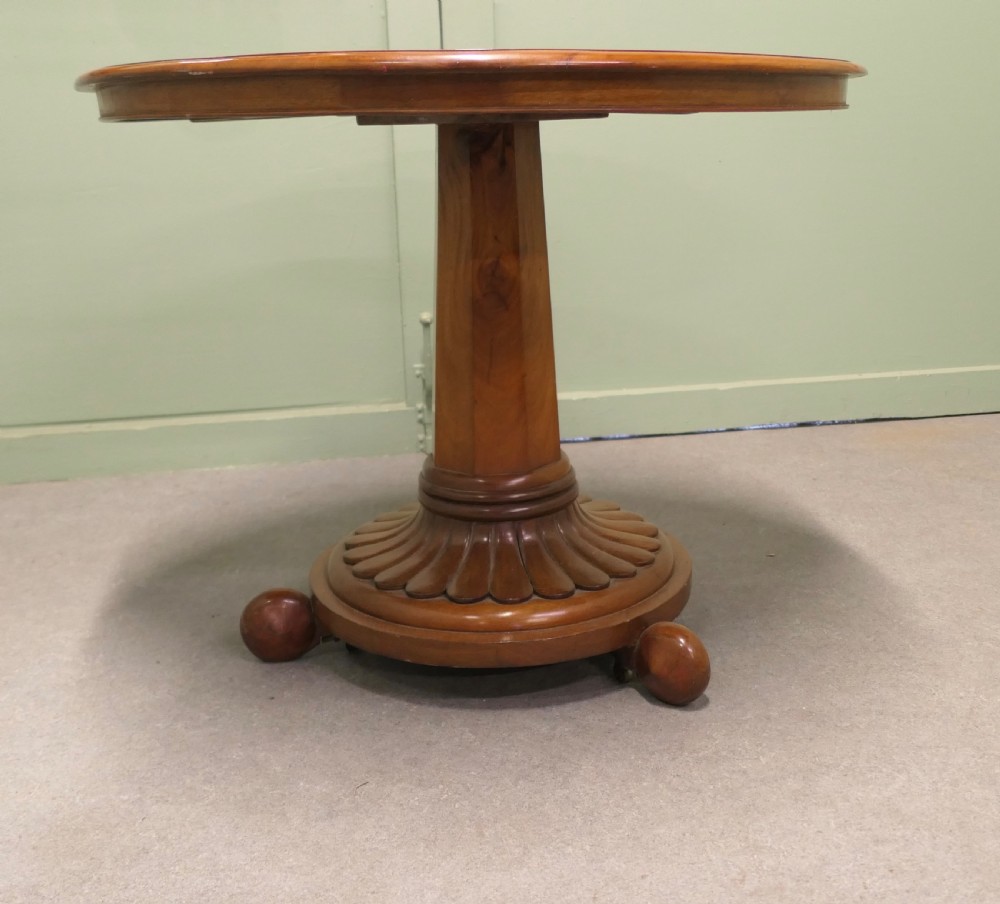 A circular cherrywood centre table featuring a polished tilt-top surface, a central stem, and a carved petal-form pedestal base on ball feet. View IV
