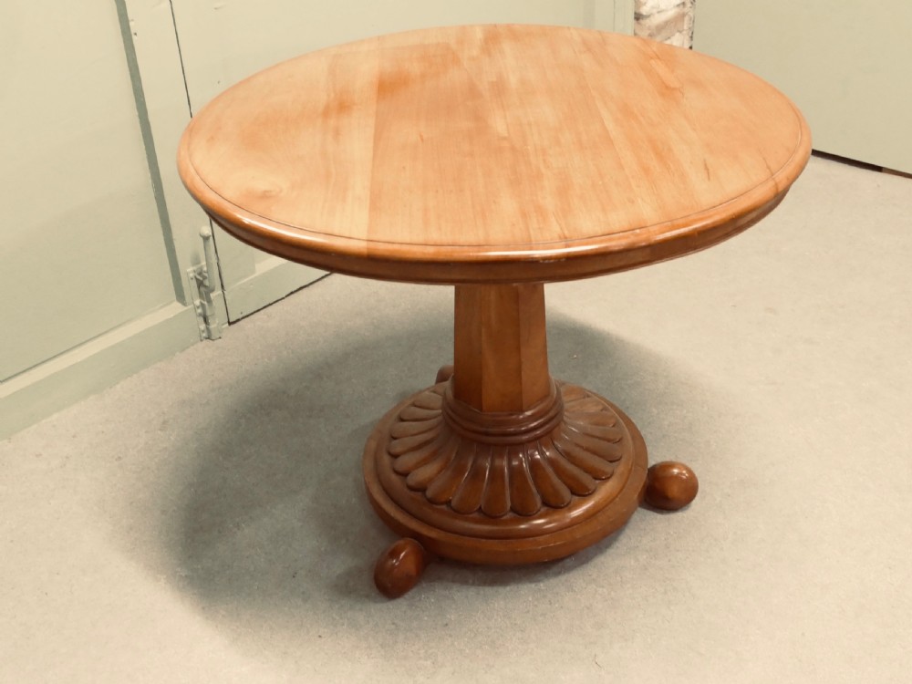 A circular cherrywood centre table featuring a polished tilt-top surface, a central stem, and a carved petal-form pedestal base on ball feet. View VI