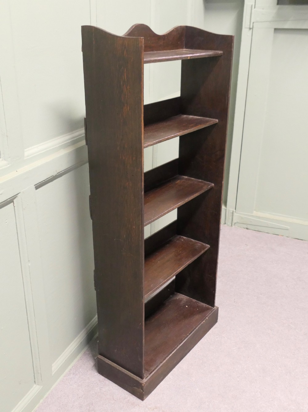 A tall dark wood Art Deco open bookcase featuring five shelves, a scalloped top rail, and a solid plinth base. View V