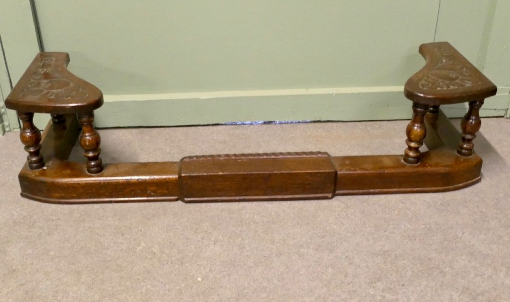 An Arts and Crafts carved oak adjustable club fender with turned baluster supports and decorative corner seats.